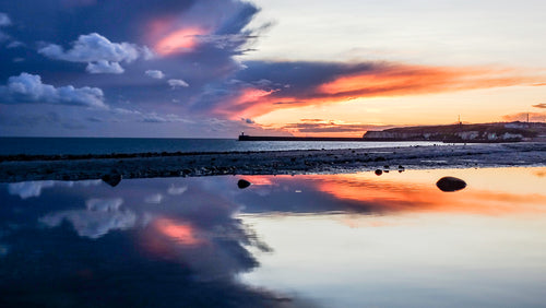 Dark storm clouds above an orange sunset reflected in still water on the Sussex coast – photograph by Sharon Maskery