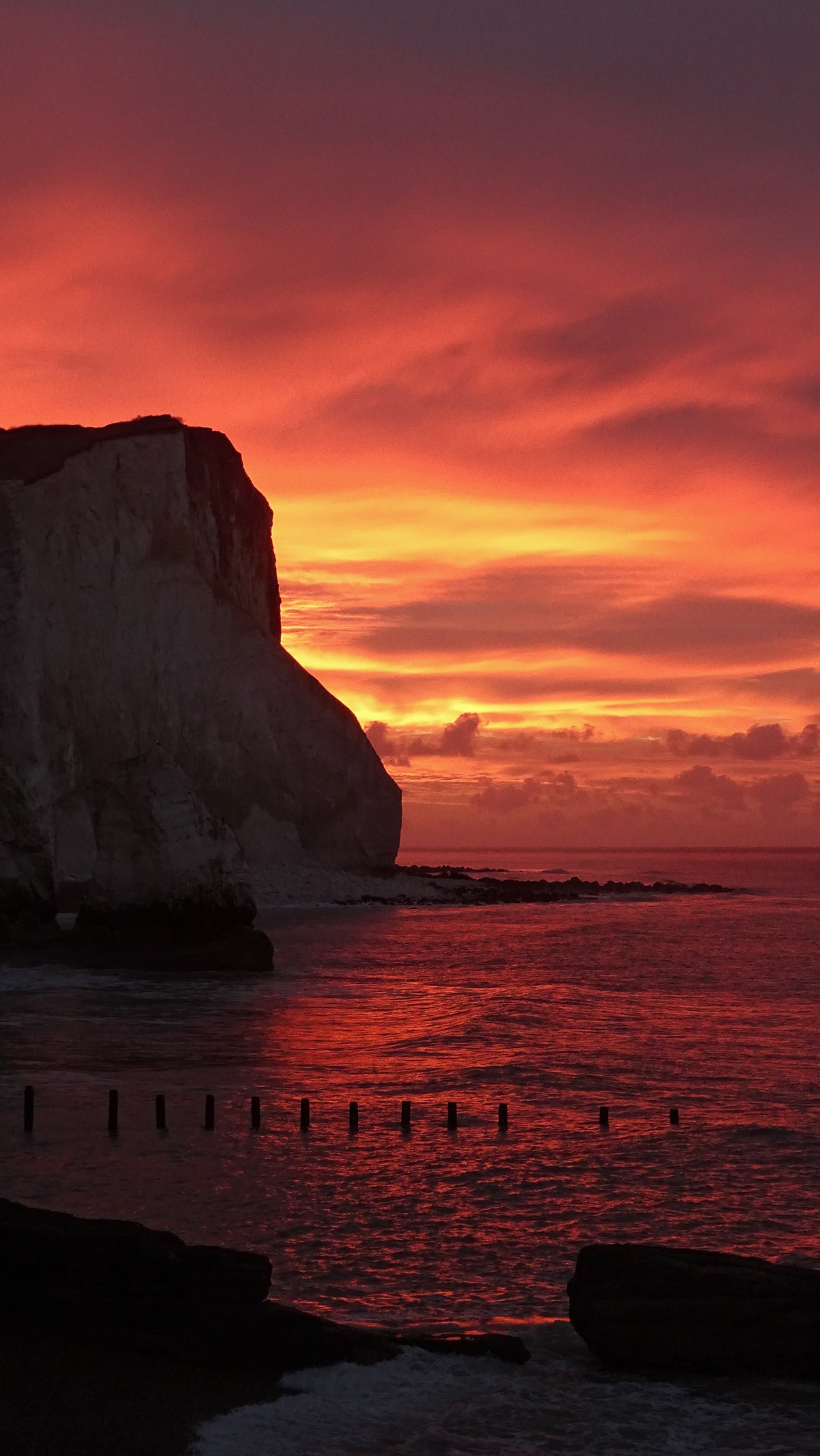 White cliffs on the Sussex coast beneath a vivid red and orange sunset reflected across the sea – original photograph by Sharon Maskery