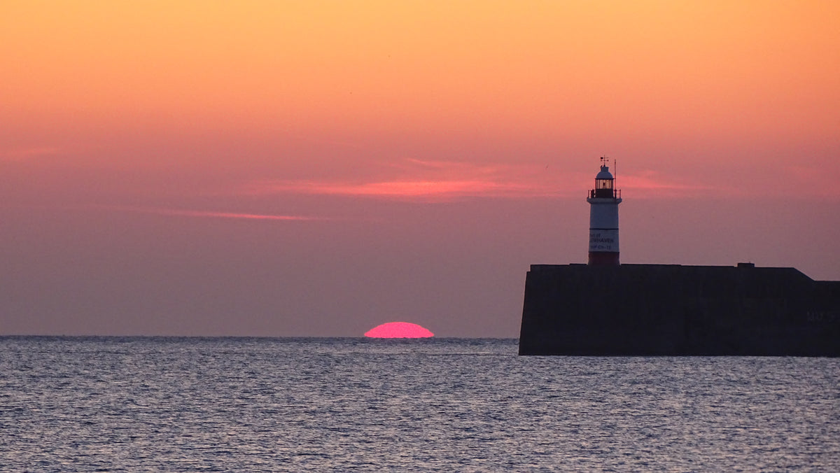 Newhaven lighthouse beside a vivid pink sunset over the Sussex coast – original coastal photograph by Sharon Maskery