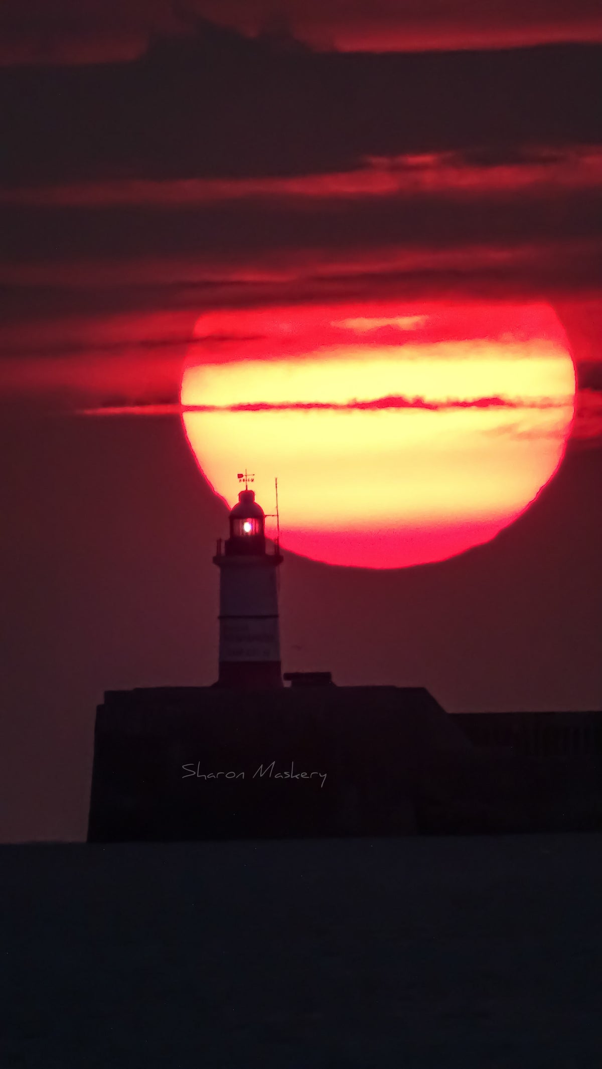 Lighthouse silhouetted against a huge red and orange sunset over the Sussex coast – original photograph by Sharon Maskery
